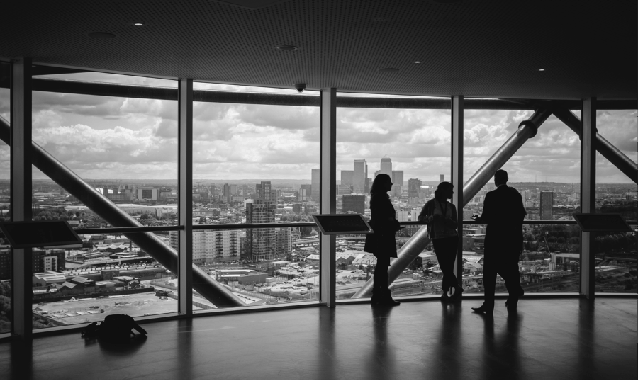 Silhouettes of four people talking inside a high-rise observation deck with large windows overlooking a city skyline.